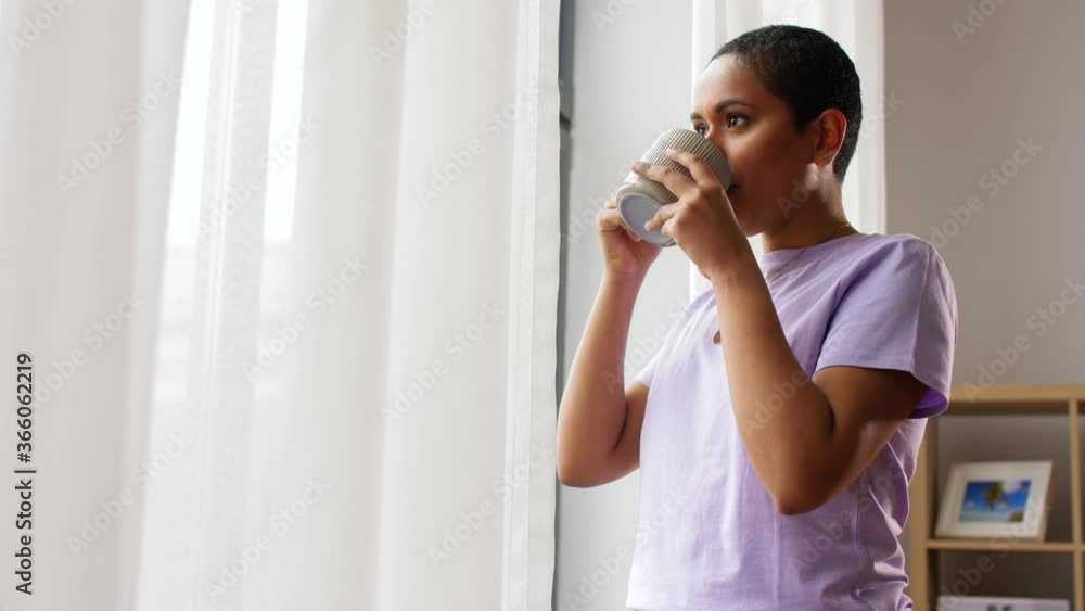 people and leisure concept - happy smiling african american woman drinking tea or coffee and looking out window at home people and leisure concept - happy smiling african american woman drinking tea or coffee and looking out window at home