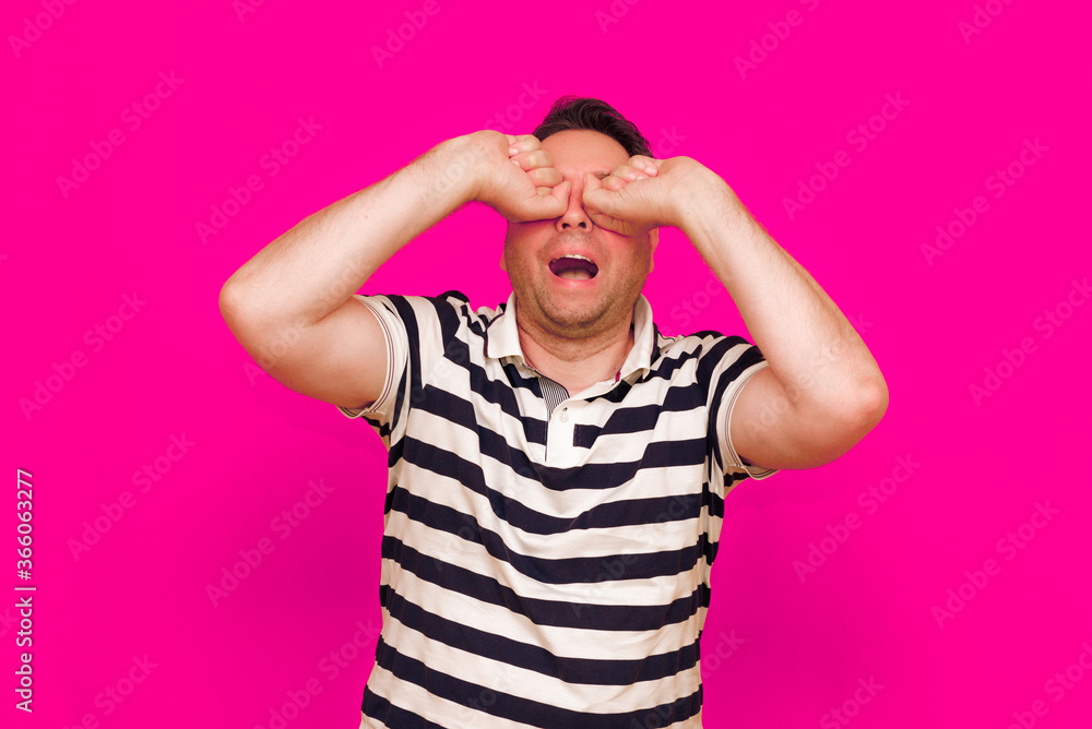 Joyful man in striped t-shirt gesturing index finger hand on camera isolated over magenta background Joyful man in striped t-shirt gesturing index finger hand on camera isolated over magenta background