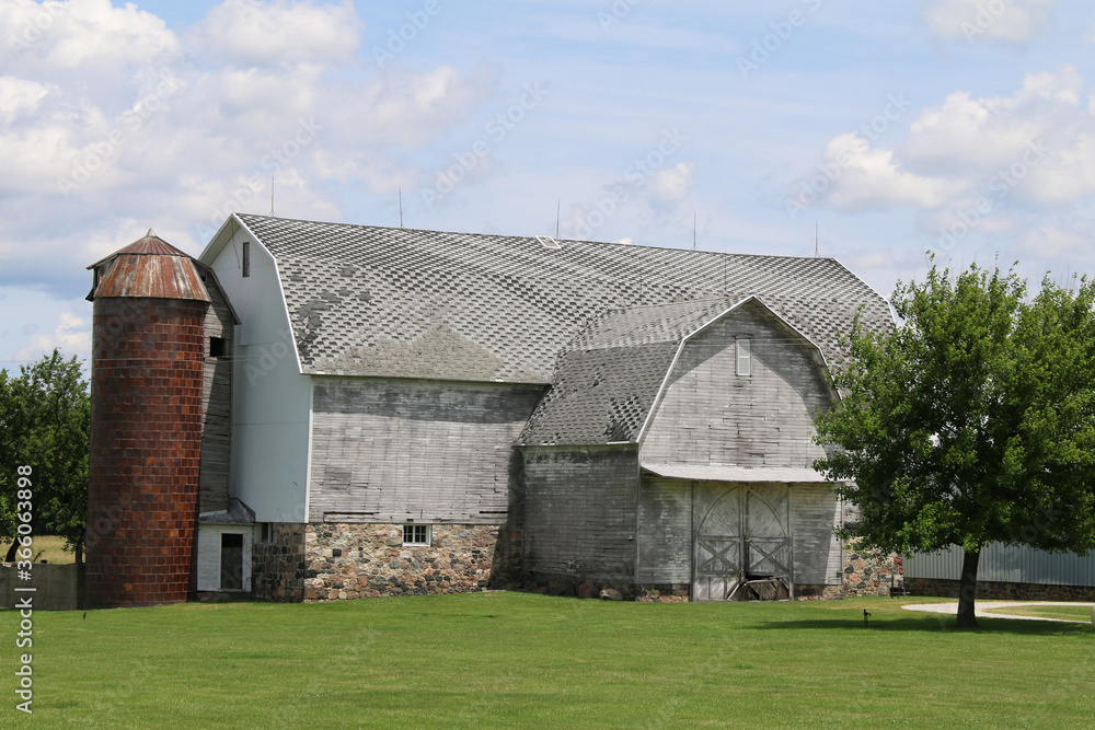 a large old stone foundation white barn and stone foundation and brick silo with a bright green grass lawn and shade trees a large old stone foundation white barn and stone foundation and brick silo with a bright green grass lawn and shade trees
