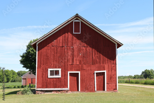 a front facing view of a wonderful old red barn with white trim and landscaped lawn with dirt road