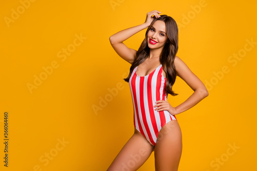 Photo of beautiful hot lady beaming smile slim figure shape bronze body arms by sides seashore life guard control wear white red striped bodysuit isolated bright yellow color background