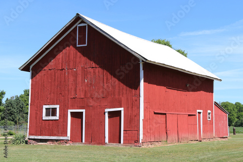 a side angle view of a red rural farm barn with white trim and landscaped lawn with bright tin roof