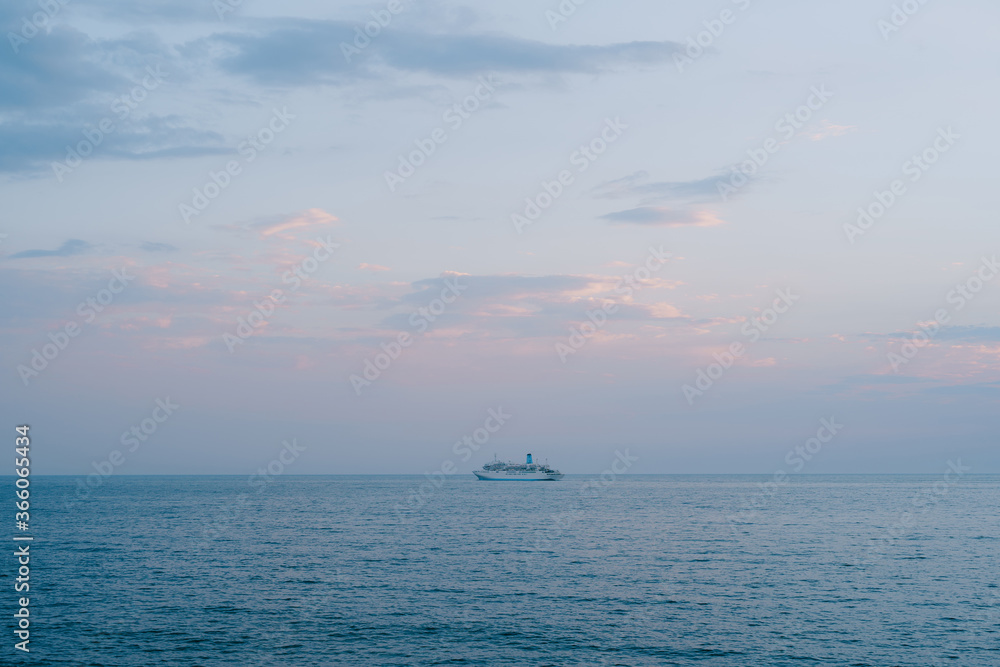 A small cruise liner sails in the open sea against the sunset sky with orange clouds.