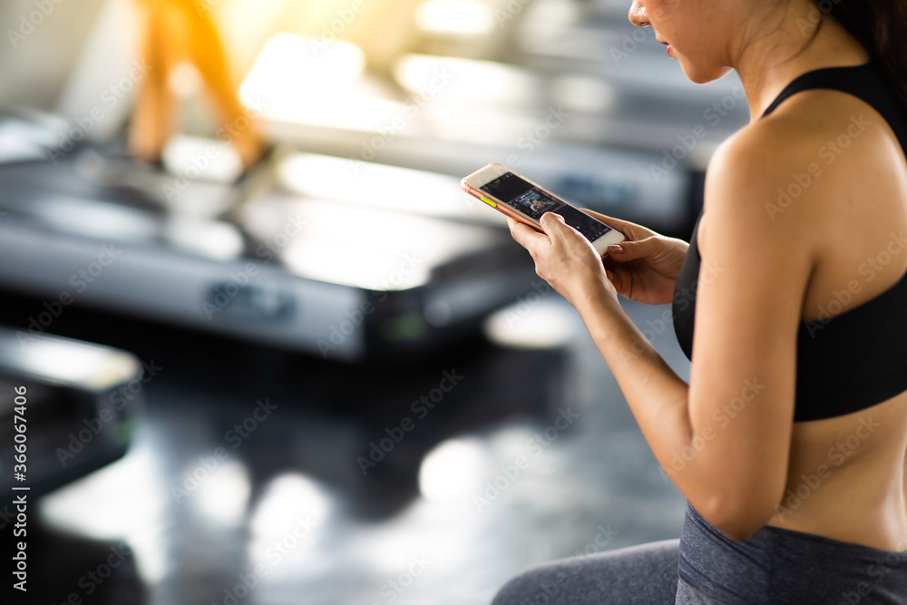 Active woman athlete taking rest and use smartphone after exercising at gym. Fitness Healthy lifestye and workout at gym concept.