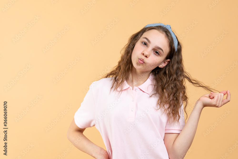 Attractive teen girl touching her curly hair looking at the camera, sending air kiss, studio portrait Attractive teen girl touching her curly hair looking at the camera, sending air kiss, studio portrait