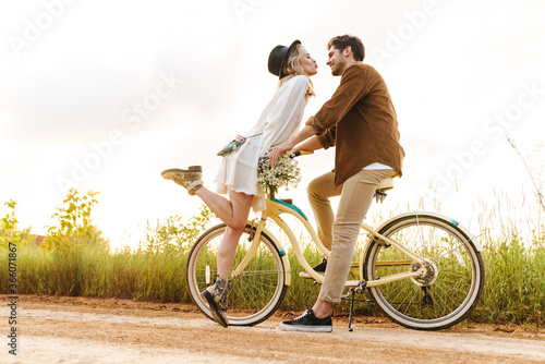 Image of young couple kissing while riding bicycle in countryside