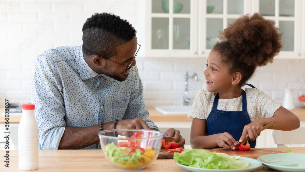 Loving happy biracial young dad teach little excited ethnic daughter cooking in morning at home, smiling african American father and small girl child prepare healthy organic vegetarian salad together Loving happy biracial young dad teach little excited ethnic daughter cooking in morning at home, smiling african American father and small girl child prepare healthy organic vegetarian salad together