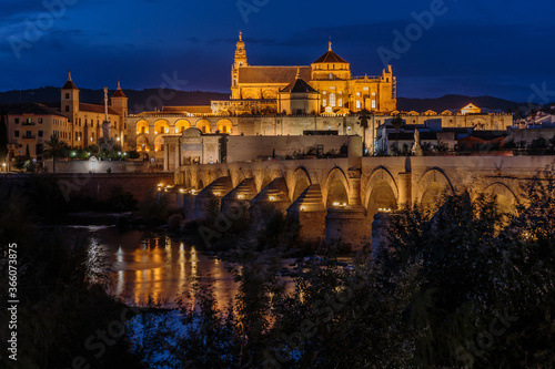 Cordoba old town in the evening at the blue hour. Mosque Cathedral with Roman bridge and river course. Illuminated buildings of the Spanish city in Andalusia
