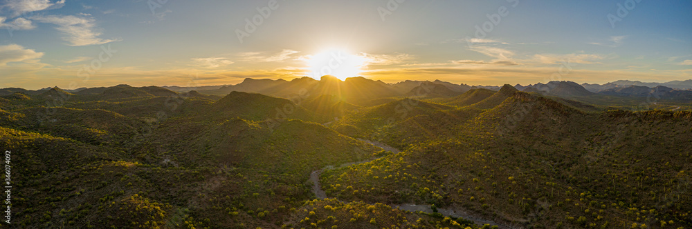 Aerial panorama over the Arizona desert during sunset with mountains and a meandering dry stream.