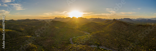 Aerial panorama over the Arizona desert during sunset with mountains and a meandering dry stream.