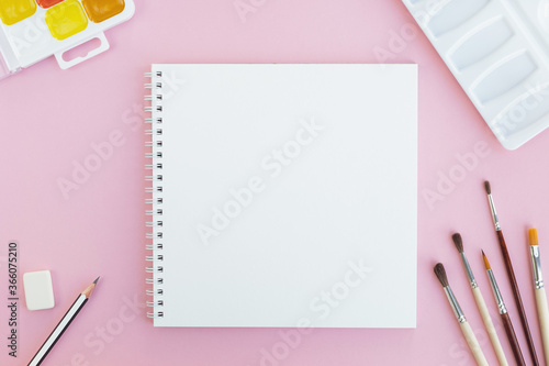 Artist workspace on pastel pink background. Empty note paper and painting supplies. Top view, flat lay, copy space
