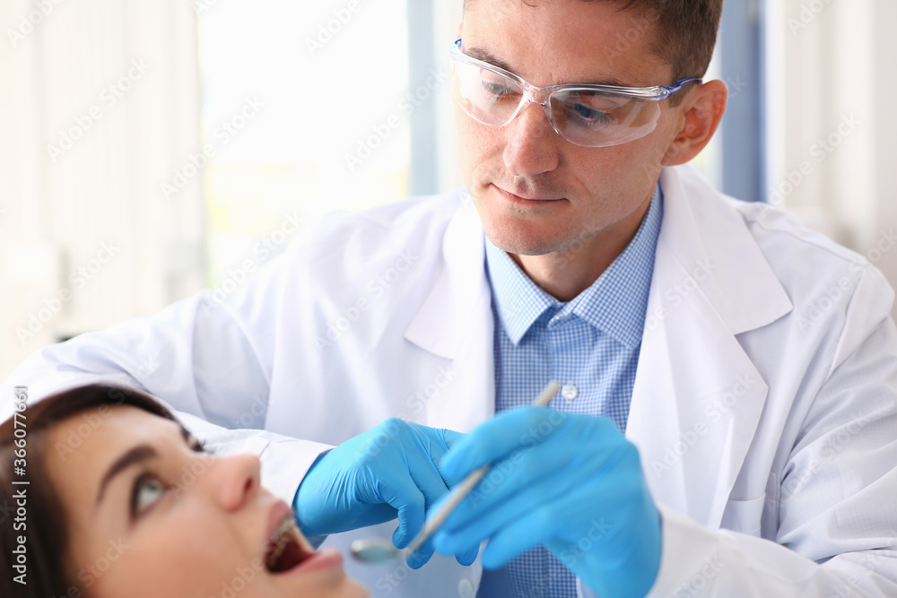 Man in protective glasses and rubber gloves is doing check up of patient using instruments Man in protective glasses and rubber gloves is doing check up of patient using instruments