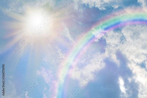 Summer sun burst and blue sky  rainbow - massive sun radiating beside fluffy clouds with a giant arcing rainbow and beautiful blue summer sky with copy space for messages
