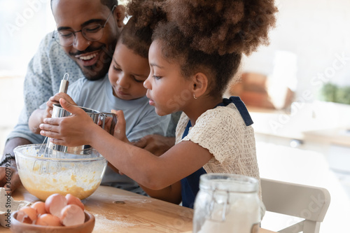 Loving african american father make dough making tasty sweet breakfast pastry with excited little children  happy biracial dad and small kids cook prepare pancakes cookies pie in kitchen together