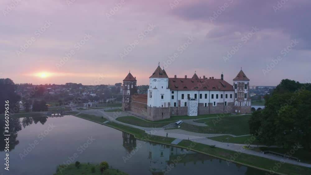 Mirsky Castle and its reflection in the lake in summer. Sunset in cloudy weather with rain clouds. Aerial view from a drone. Mirsky Castle and its reflection in the lake in summer. Sunset in cloudy weather with rain clouds. Aerial view from a drone.