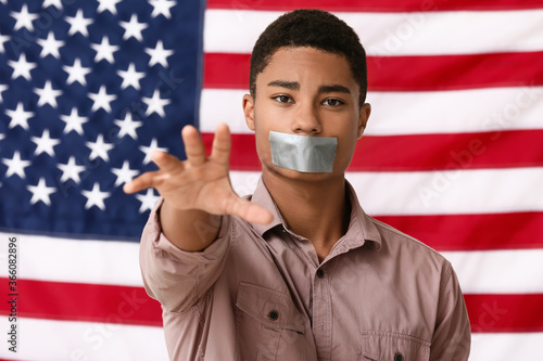 Foto Sad African-American teenage boy with taped mouth near national flag of USA