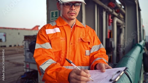 Filipino deck Officer on deck of offshore vessel or ship , wearing PPE personal protective equipment. He fills checklist. Paperwork at sea photo