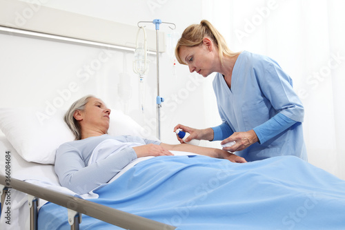 elderly woman lying in the hospital room bed, nurse disinfect the patient's arm to insert the drip