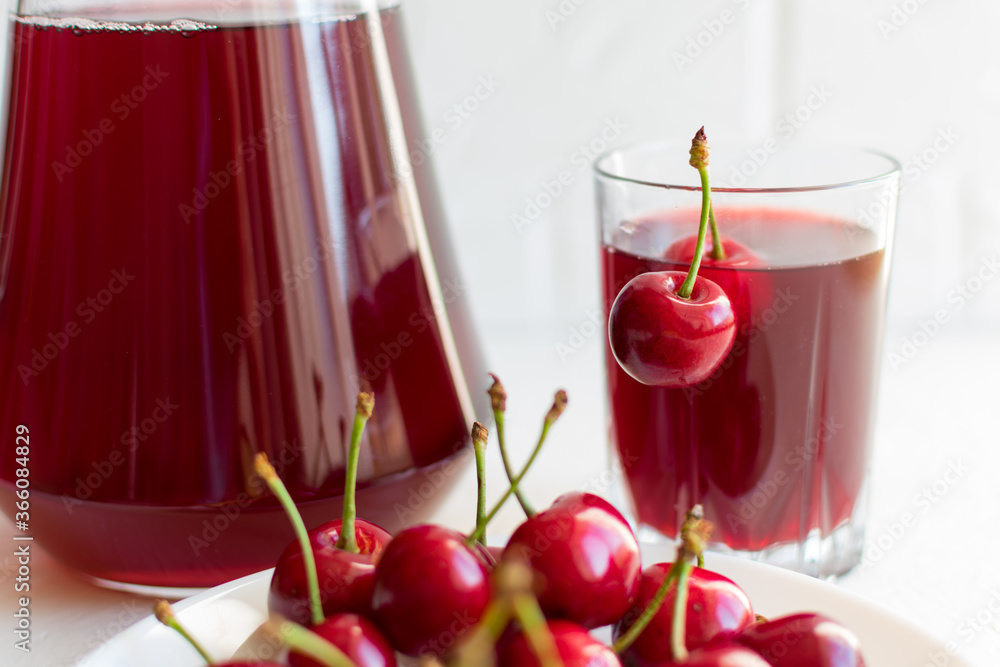 Cherry juice in a glass cup with cherry berries on a plate on a gray table. Selective focus. Cherry juice in a glass cup with cherry berries on a plate on a gray table. Selective focus.