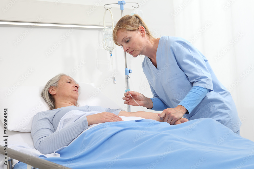 Obraz premium elderly woman lying in the hospital room bed, nurse holding the needle to connect the IV to the patient's arm