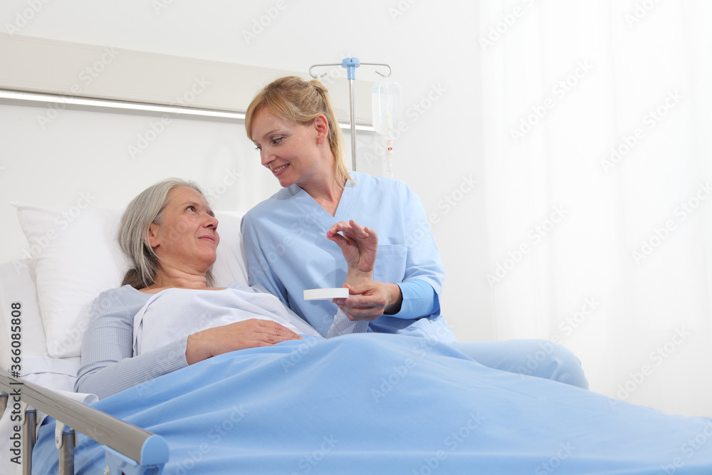 Obraz premium nurse gives the pill to the elderly woman patient lying in the hospital room bed, concept of loneliness and old age diseases