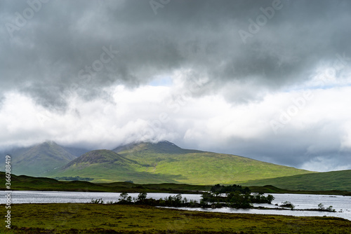 Scottish highlands mountain under heavy clouds with trees on the lake in the front plan.