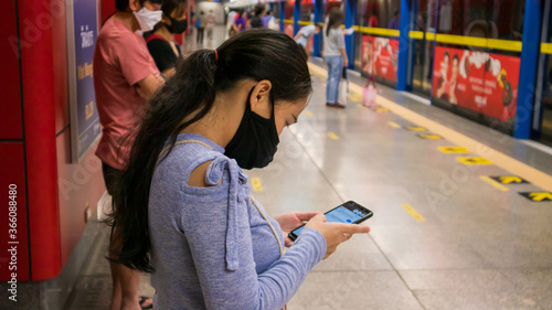 Woman wearing a mask to protect the virus, Covid-19, who is using a smartphone while waiting to travel