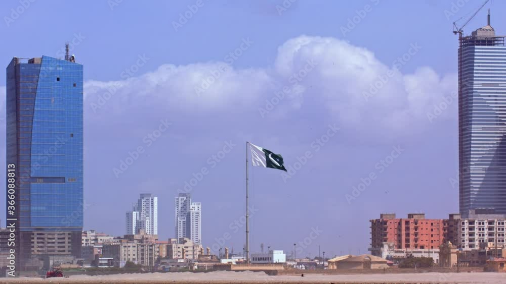 Pakistan's National flag (Public Property) waving on the beach of Karachi. Symmetry shot shows two high-rise buildings in the background. Pakistan's National flag (Public Property) waving on the beach of Karachi. Symmetry shot shows two high-rise buildings in the background.