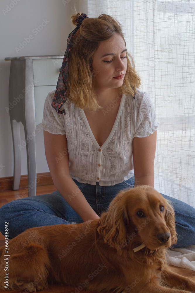 Chica con su perro sentada en el suelo de madera mirando por la ventana