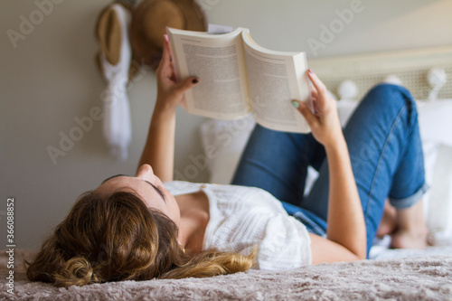 Chica tumbada en la cama leyendo un libro en su habitación photo