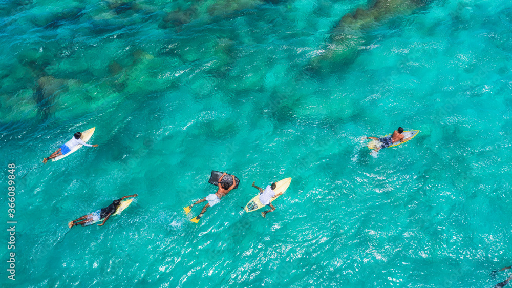 Aerial pic of surfers waiting for the next big wave in the middle of the ocean in Maldives paradise.