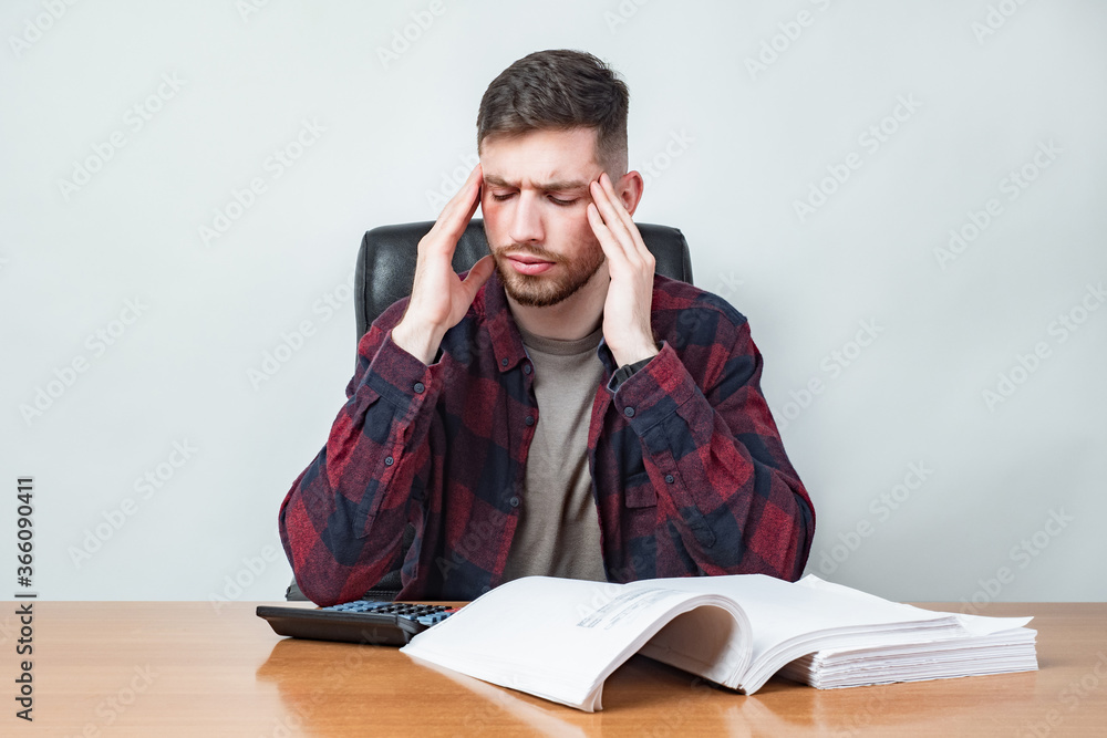 Man is upset. Concept - headache from reading. Concept - fatigue at work. Man is counting expenses. Big contract and calculator on table. Guy holds his head. Man has stress due to financial situation Man is upset. Concept - headache from reading. Concept - fatigue at work. Man is counting expenses. Big contract and calculator on table. Guy holds his head. Man has stress due to financial situation
