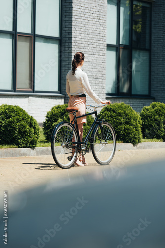 Fototapeta Naklejka Na Ścianę i Meble -  selective focus of businesswoman walking with bicycle near modern building