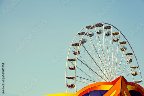 Retro toned picture of a Ferris wheel in an amusement park with cloudless sky, space for text.