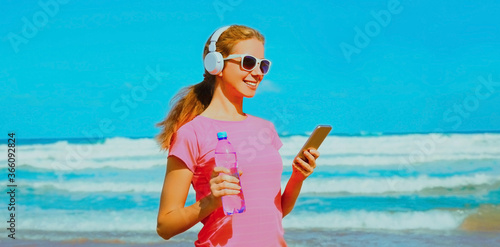 Fitness woman with phone listening to music on the beach