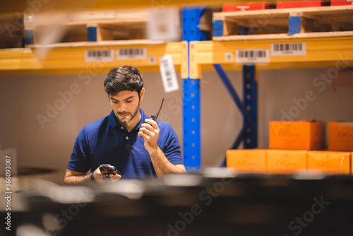 Male dispatcher, warehouse worker checking packages while using walkie-talkie in distribution warehouse storage. photo