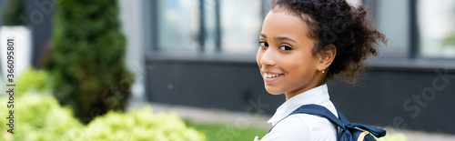 smiling african american schoolgirl with backpack outdoors, panoramic shot