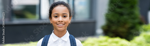 smiling african american schoolgirl with backpack outdoors, panoramic shot