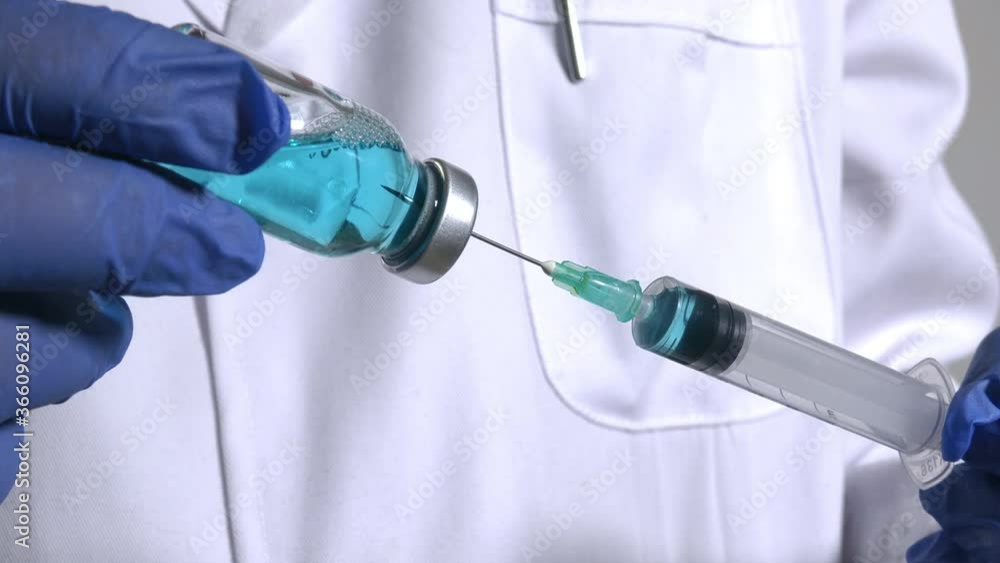 Medical analyst injects a glass vial with blue liquid into a syringe. Vaccine and Covid experiment Medical analyst injects a glass vial with blue liquid into a syringe. Vaccine and Covid experiment