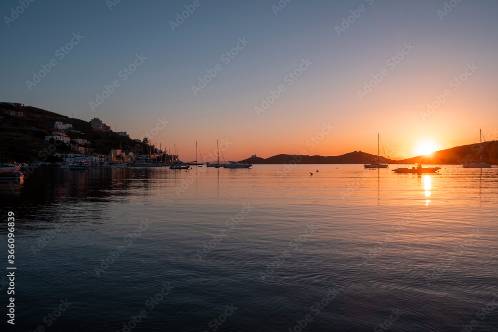 Sunset orange color over sea water. Boats anchored at Vourkari port, Kea island, Greece.