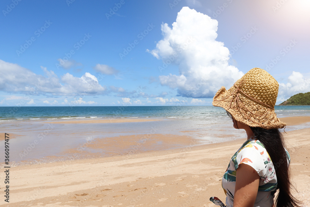 Outdoor summer portrait of young pretty woman looking to the ocean at tropical beach, enjoy her freedom and fresh air, wearing stylish hat and clothes on Vacation.