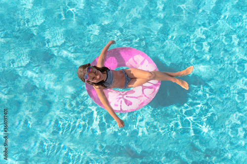 Happy girl in bikini in the swimming pool. Child on the inflatable mattress. Lovely teenager sunbathes and playing in blue water. Summer vacations.