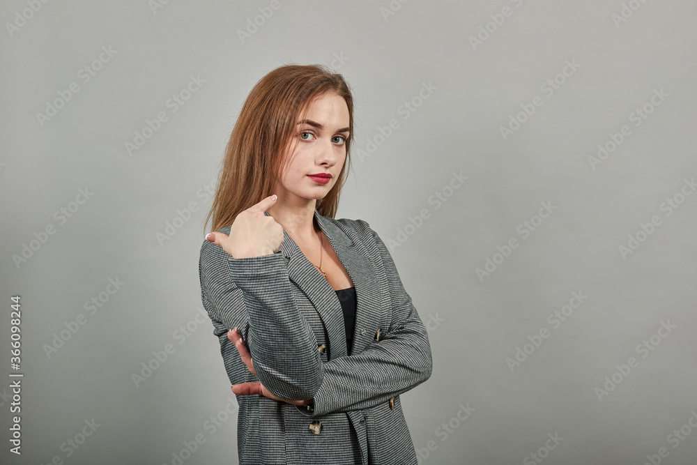 Pointing with hand at chest and staring. Shocked facial expression. Young attractive woman, dressed gray jacket, with green eyes, light brown hair, background Pointing with hand at chest and staring. Shocked facial expression. Young attractive woman, dressed gray jacket, with green eyes, light brown hair, background