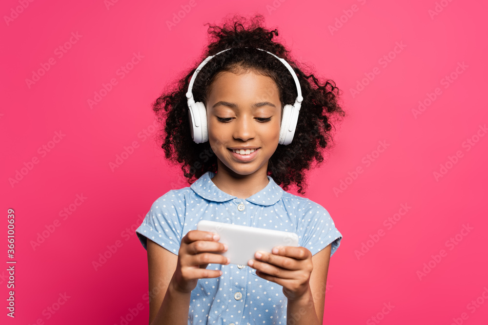 smiling curly african american kid in headphones using smartphone isolated on pink smiling curly african american kid in headphones using smartphone isolated on pink
