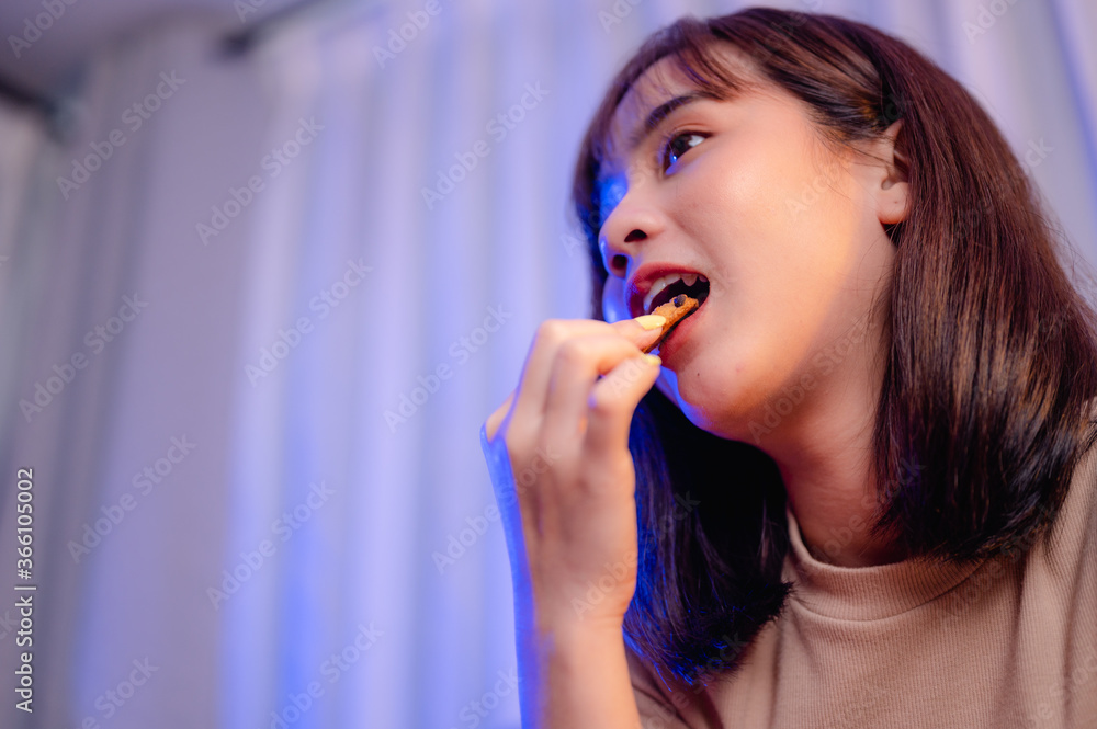 Young woman while watching TV, relaxing, eating snack and cookie by ordering delivery, at home on holiday. junk food, unhealthy meal, obesity risk. Young woman while watching TV, relaxing, eating snack and cookie by ordering delivery, at home on holiday. junk food, unhealthy meal, obesity risk.