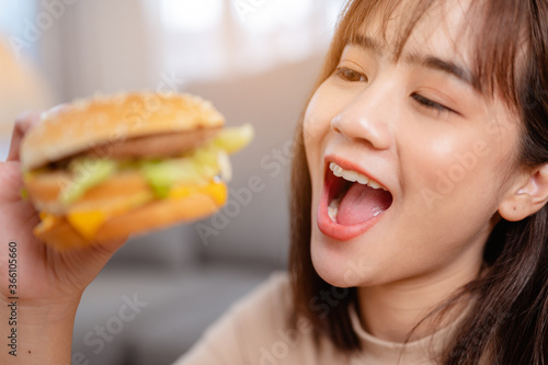 Hungry young woman eating junk food hamburger and pizza for lunch by ordering delivery at home on holiday. unhealthy meal  obesity risk.