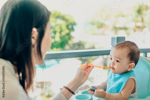 Asian 7 months baby boy eating blend food on a high chair  Mother  feeds a Little Baby with a Spoonful of food.