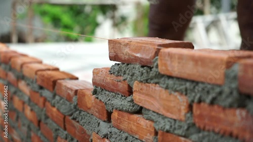 Hands of workman with trowel builds the wall by bricklaying the red bricks with cement