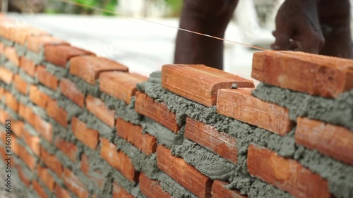 Hands of workman with trowel builds the wall by bricklaying the red bricks with cement