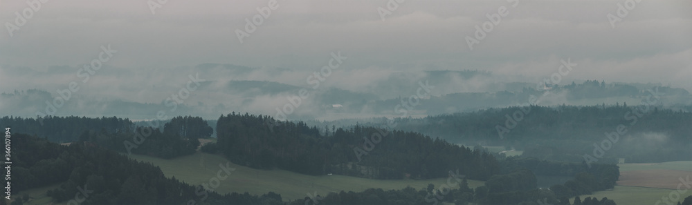 Panoramic view to forest, meadow silhouette with misty fog. Czech landscape
